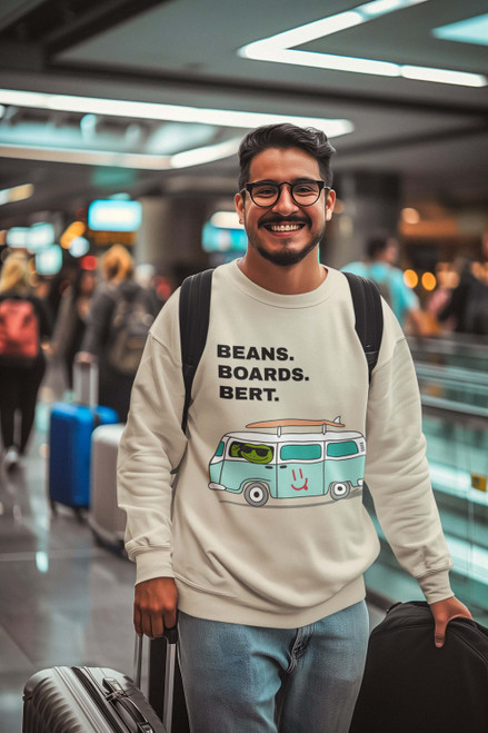 Smiling traveler at airport in cream Beans. Boards. Bert. – Surf Van Crew by Coo Coo’s Coffee — cozy unisex sweatshirt with Bert driving a teal surf van graphic