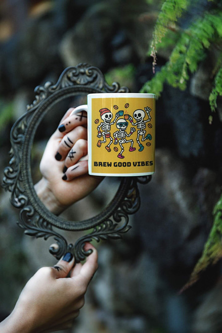 Brew Good Vibes dancing skeletons mug reflected in an ornate handheld mirror outdoors.