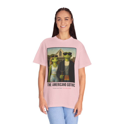 The Americano Gothic coffee tee — two geckos posed as the couple from Grant Wood's American Gothic in front of a white gothic-window farmhouse; Bert in sunglasses holding a pitchfork, Gertie in pearls beside him, with "The Americano Gothic" and a red Florida Brew Crew line beneath — Coo Coo's Coffee Brew Good Vibes garment-dyed Comfort Colors art parody tee.