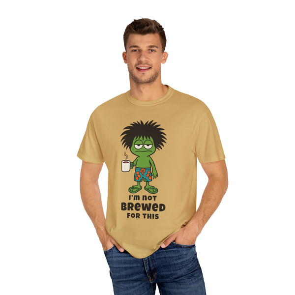 I’m Not Brewed for This – Frazzled Bert Tee by Coo Coo’s Coffee in Mustard yellow. Features a tired gecko clutching coffee, bold black text, and relaxed unisex fit. Male Model