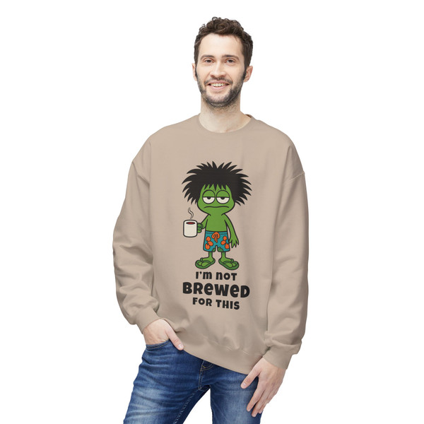 “I’m Not Brewed for This – Frazzled Gecko Sweatshirt in Sand by Coo Coo’s Coffee. Neutral sand tone pullover with Bert the frazzled gecko, made for coffee lovers who aren’t ready to function without their brew.” Male model