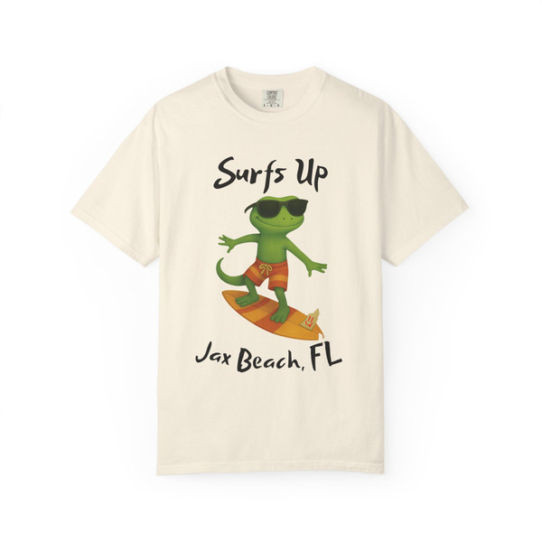 Ivory short-sleeve tee featuring Bert the gecko surfing on an orange board with “Surfs Up – Jax Beach, FL” text, Bert’s Surf Club – Jax Beach Tee by Coo Coo’s Coffee.