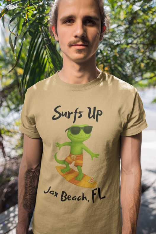 Man wearing the Bert’s Surf Club – Jax Beach Tee in mustard color, standing outdoors with palm plants in the background, showcasing the surfing gecko design.