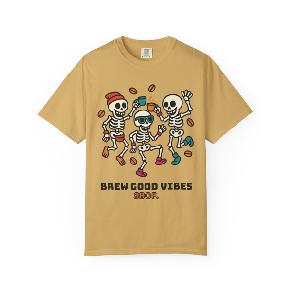 “Mustard yellow tee featuring playful skeletons dancing with coffee beans, design reads ‘Brew Good Vibes – Coo Coo’s Coffee.’”