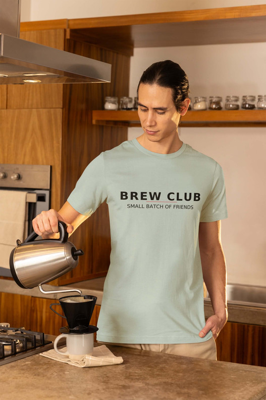 Man wearing light Brew Club – Small Batch Society Tee by Coo Coo’s Coffee while making a pour-over — minimalist coffee shirt celebrating community and craft brewing
