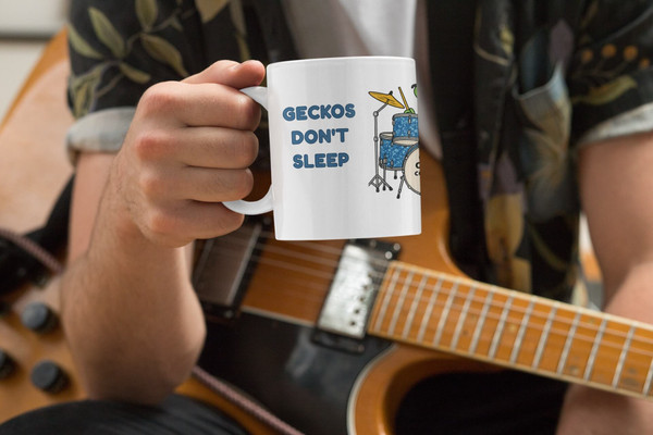 Person holding Geckos Don’t Sleep, They Drum! mug while playing guitar — music & coffee vibes — Coo Coo’s Coffee