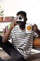 Man sitting on the floor in a striped shirt holding a camera and the Caffeine Cyclone – Molecule of Madness Mug by Coo Coo’s Coffee, featuring a bold caffeine molecule design