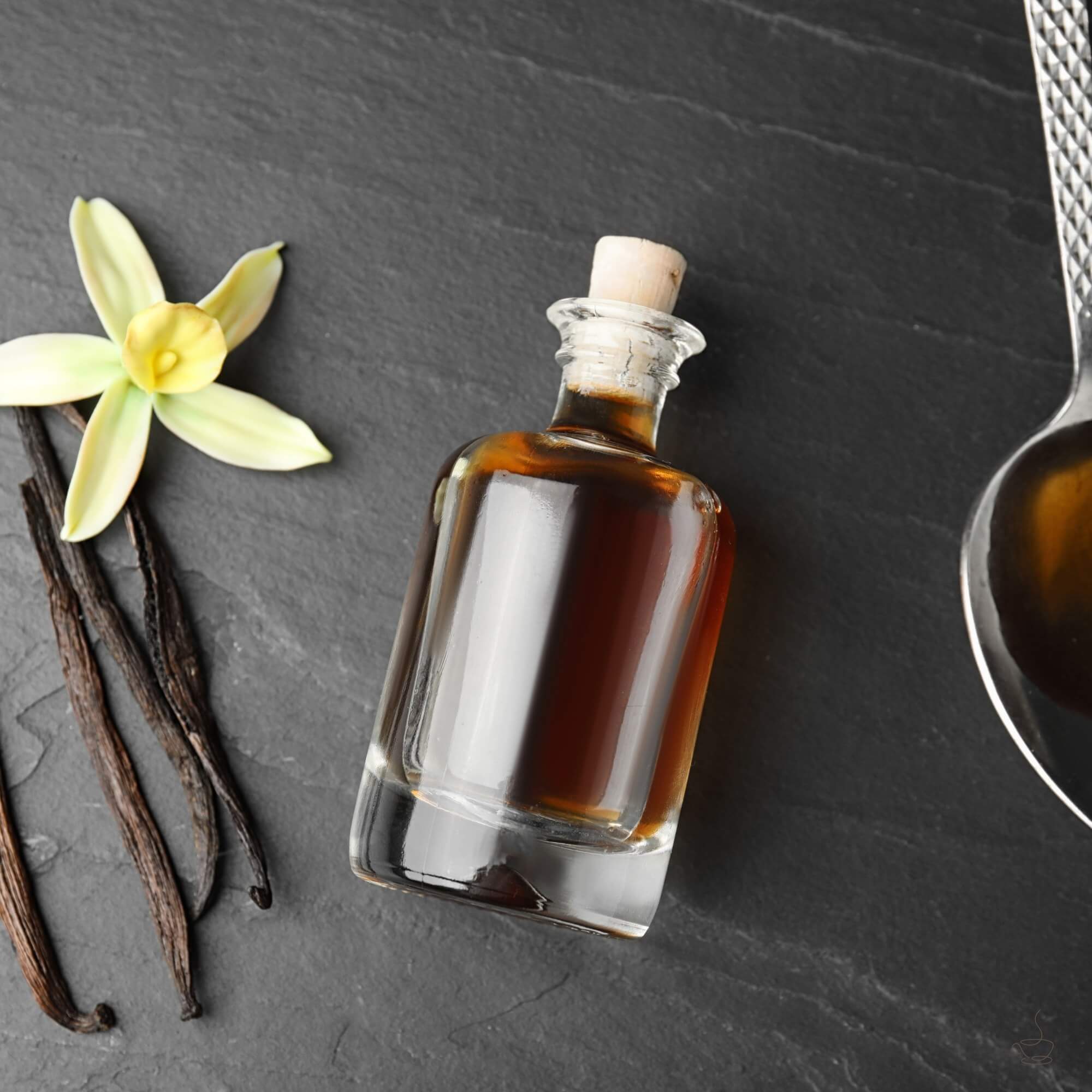 Small bottle of vanilla syrup next to a cup of coffee