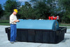A worker inspecting a blue tank placed in a black containment sump outdoors.