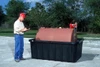 A worker inspecting a red container placed in a black containment sump outdoors.