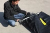 A man kneeling on a gravel surface attaching a metal support to a black flexible containment sump.
