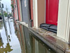 Flooded city street with black water barrier bags stacked at the base of a red door to block rising water from entering the building.