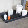 A black utility tray holding various containers, including white buckets, small plastic bottles, and a paint can, against a concrete wall.