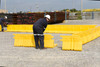 Workers assembling yellow containment wall panels on a gravel lot.