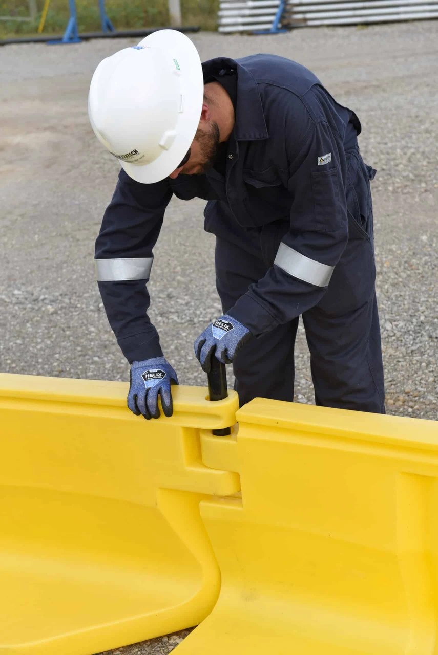 Worker securing a connection between two yellow containment wall panels.
