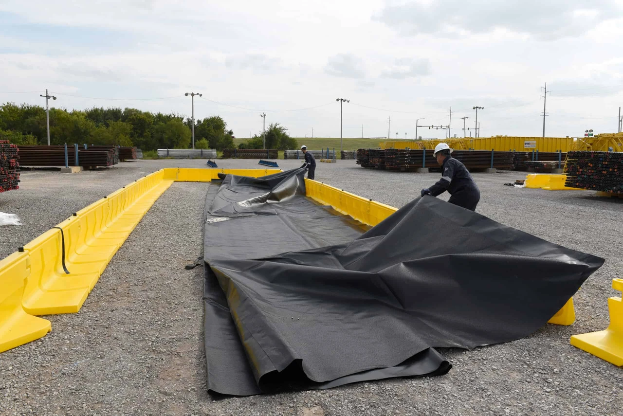 Workers spreading a black liner inside the yellow containment walls.
