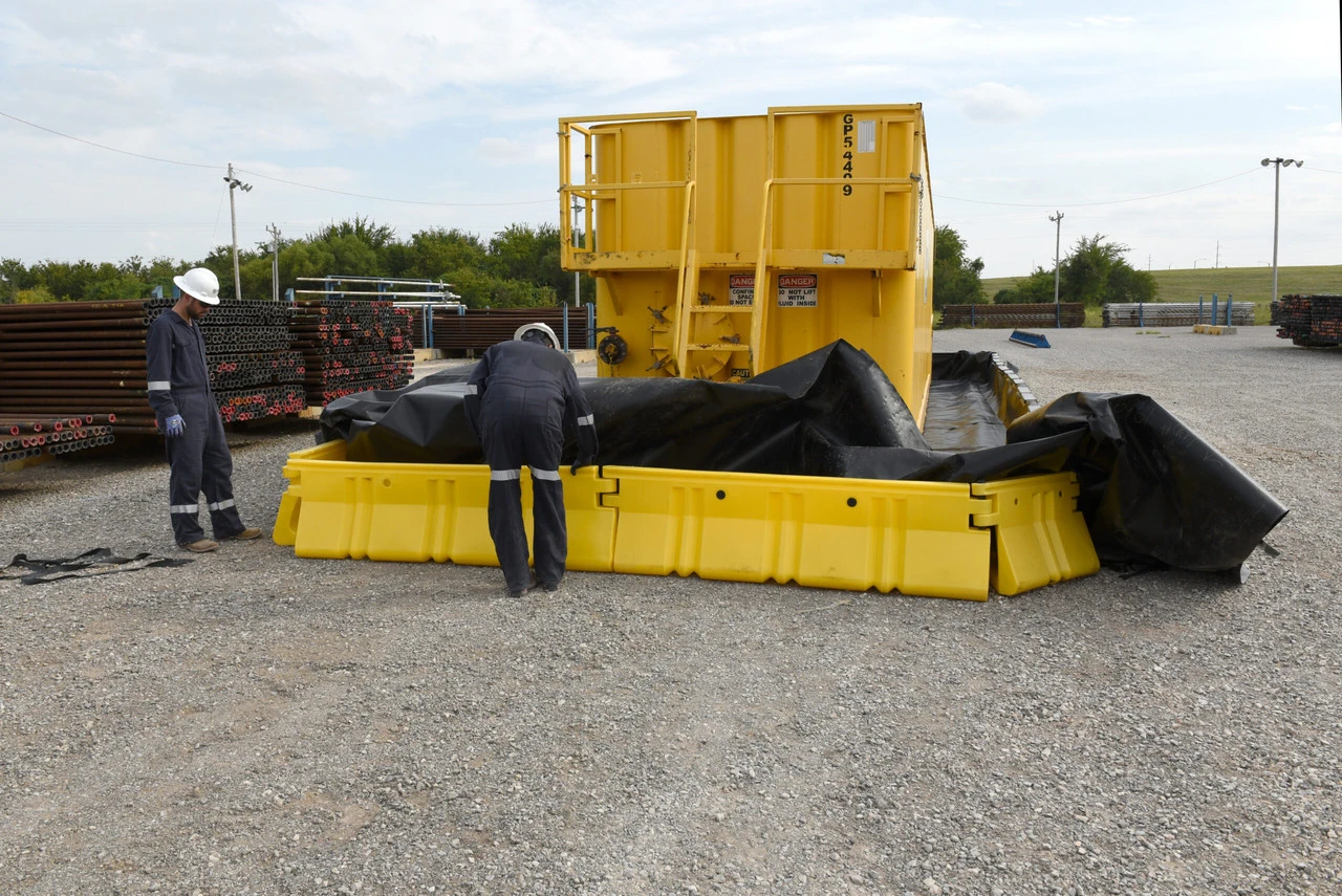 Workers adjusting a containment wall system around a yellow container.