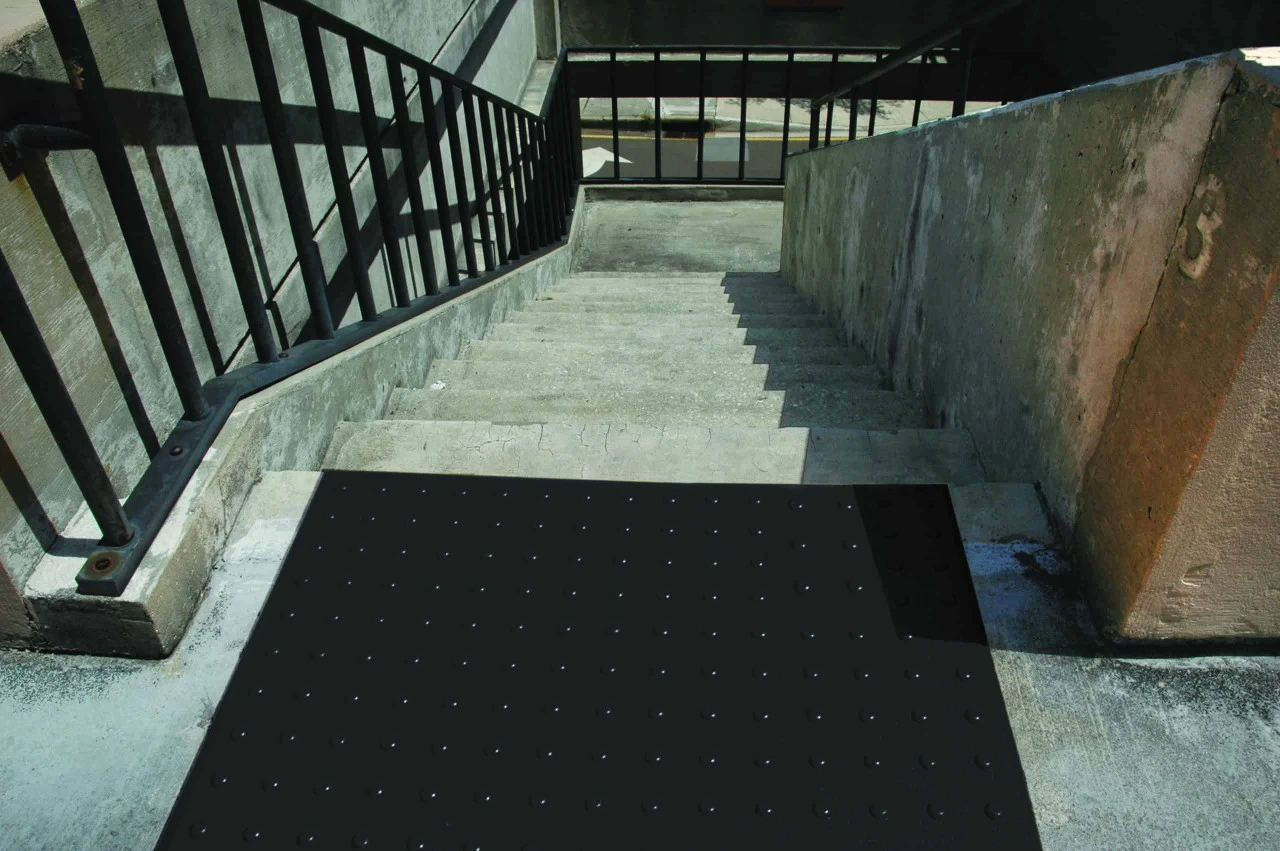Black tactile ADA pad installed at the top of a stairway, ensuring safety and accessibility.