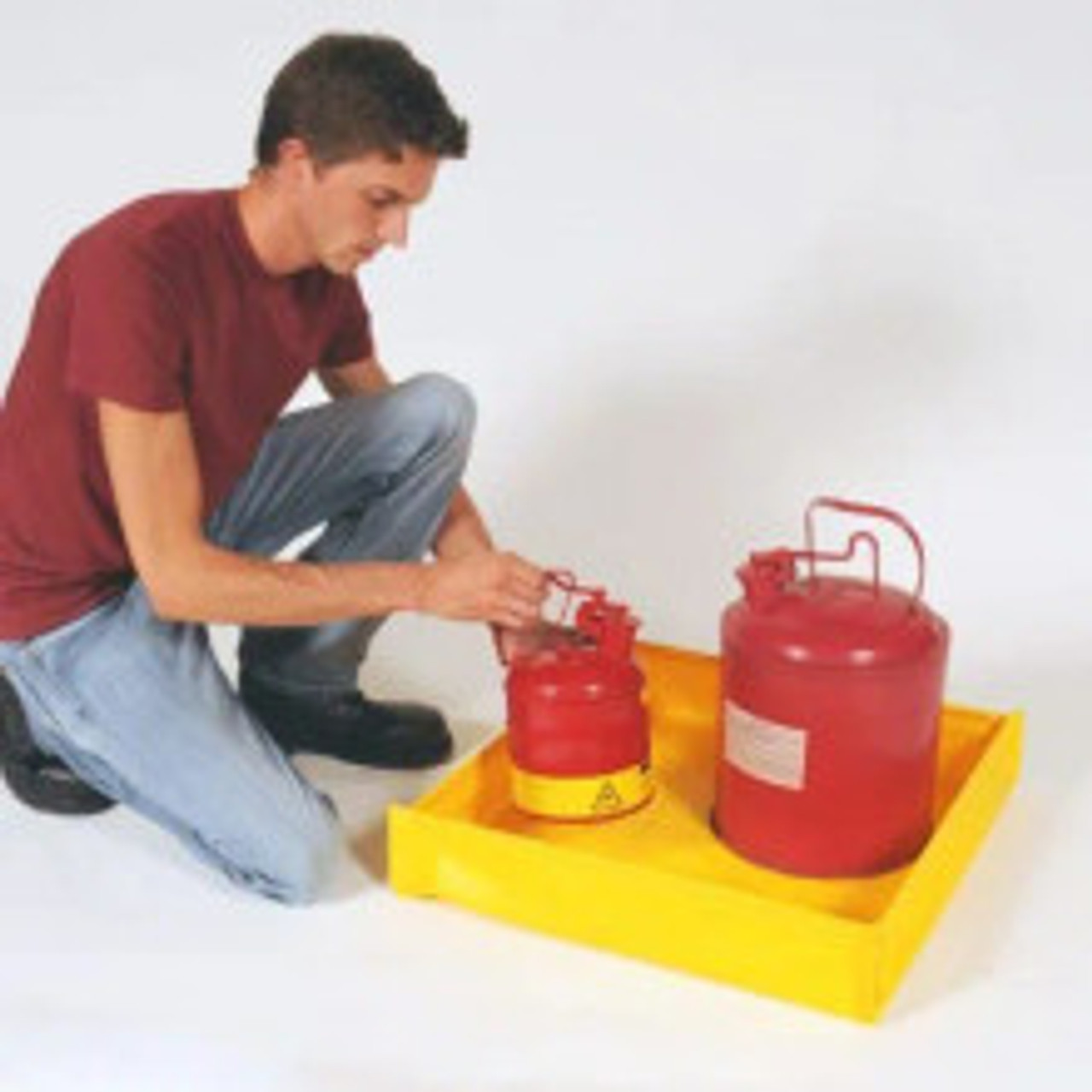 Man placing red safety cans into a yellow utility tray, demonstrating its spill containment capabilities.