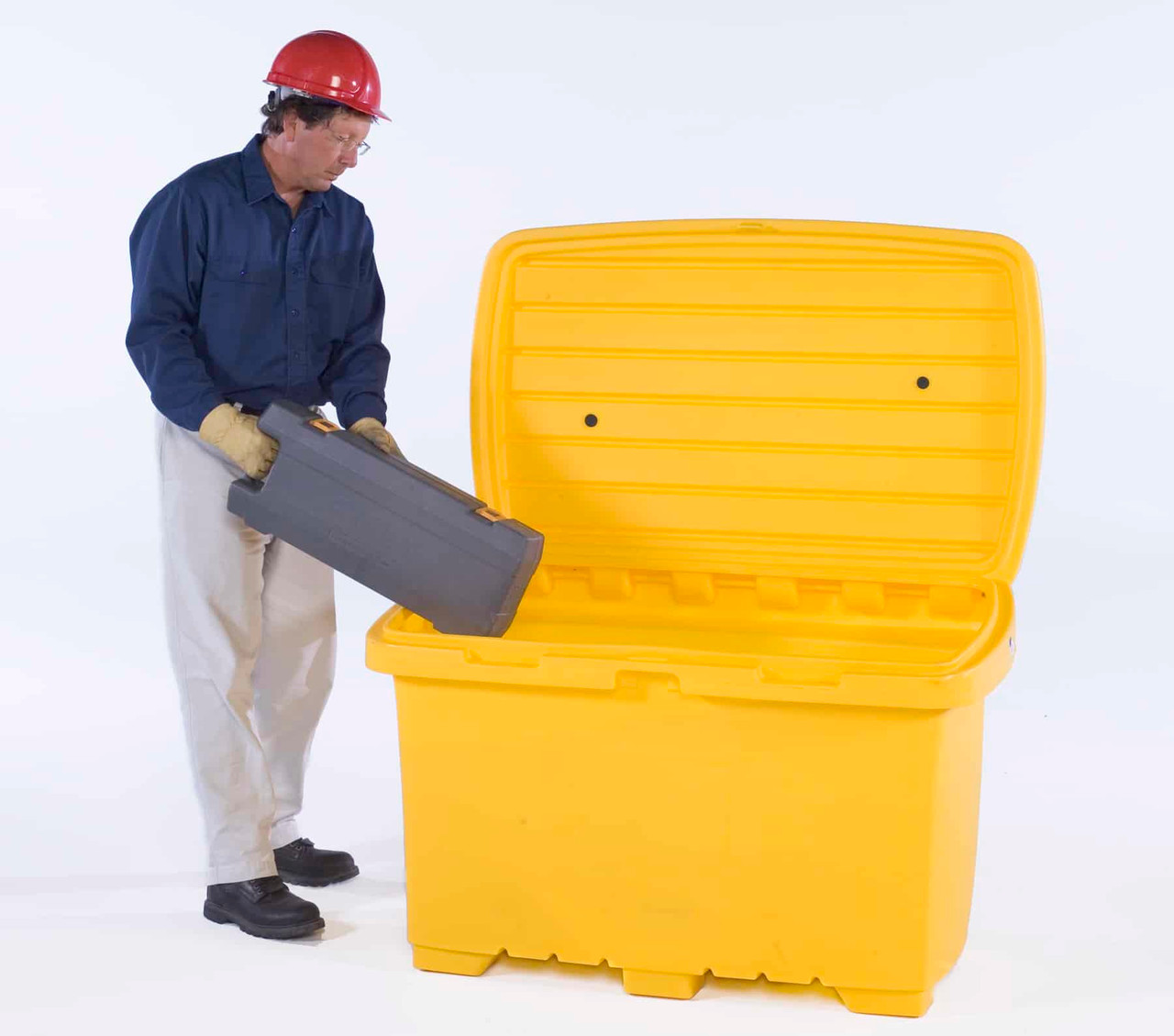 A man wearing a red hard hat and gloves placing a toolbox inside a yellow utility storage box with an open lid, showcasing its functionality.