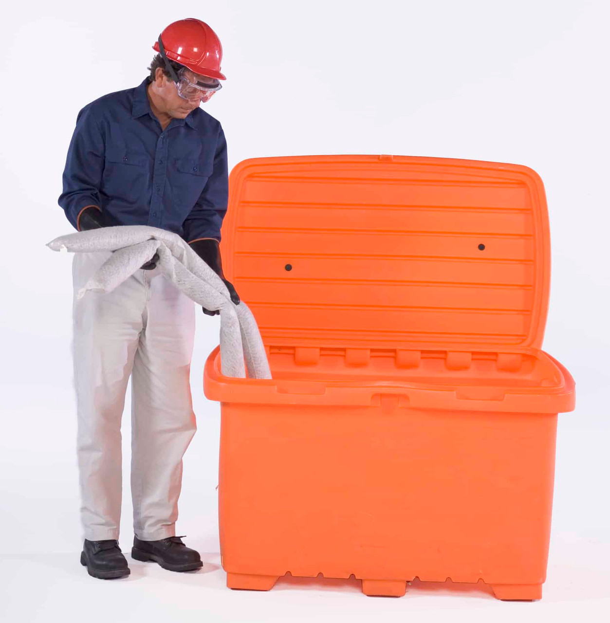 A man wearing a red hard hat and safety goggles placing absorbent materials into an orange utility box with an open lid, demonstrating its capacity.