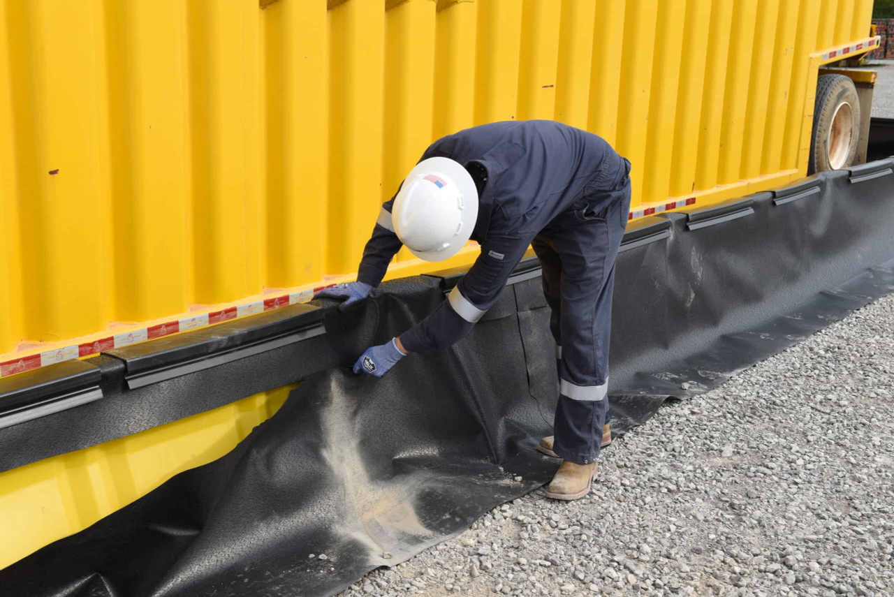 Worker securing a black liner to a yellow containment wall.