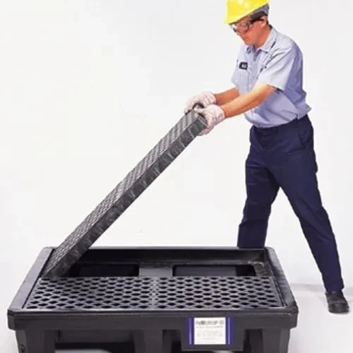 A worker in a hard hat and safety gloves lifting the grating of a black spill containment pallet to access the interior for maintenance or cleaning.