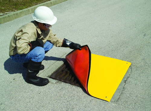 A worker in safety gear lifting the edge of a yellow drain seal while covering a metal drain grate on a roadway.
