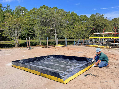 Man setting up a containment berm outdoors - A worker in a hard hat and gloves installs wire brackets to set up a black and yellow containment berm on a dirt surface.