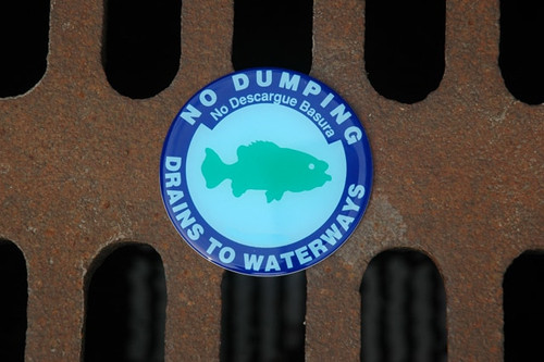 No Dumping, Drains to Waterways" marker with a fish illustration attached to a metal storm drain. No Dumping, Drains to Waterways" marker with a fish illustration attached to a metal storm drain.