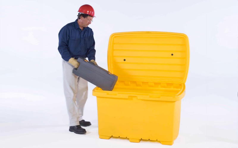 Construction worker putting tool box into large yellow storage container
