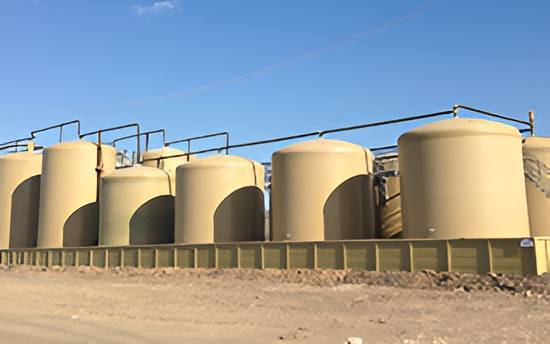 A row of large beige fiberglass storage tanks used for industrial water and chemical storage, providing corrosion-resistant and durable containment solutions.