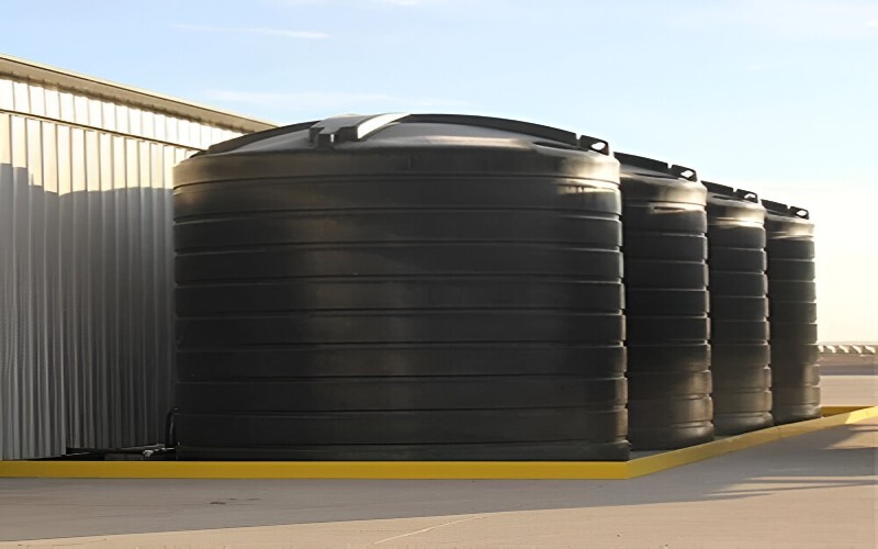 Black flat-bottom storage tanks installed outdoors beside a building.
