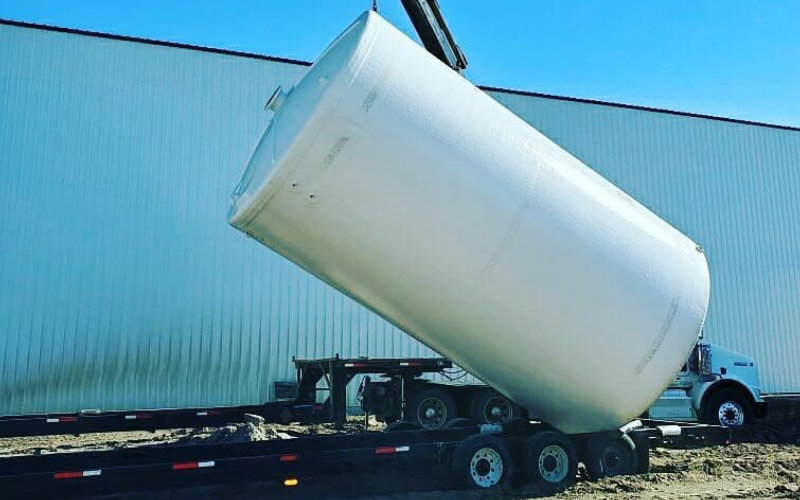 a white fiberglass tank being installed with a crane