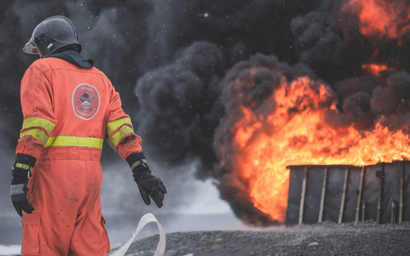 Firefighter looking toward a massive fire that’s emitting thick, dark smoke
