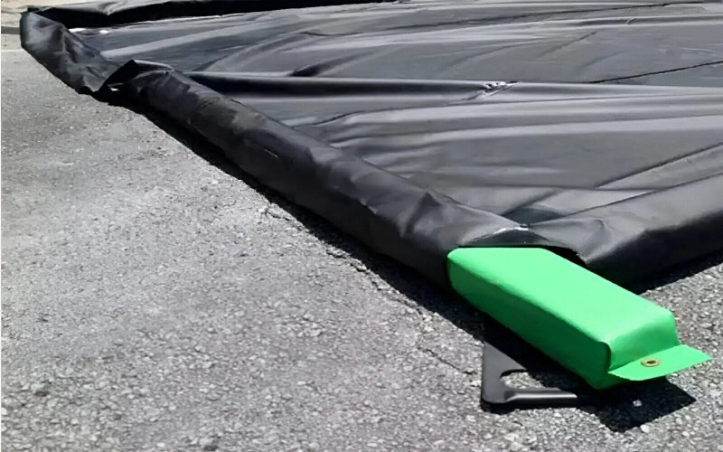 Close-up of a green strap securing a black containment liner on an asphalt surface, showing durability and secure attachment.