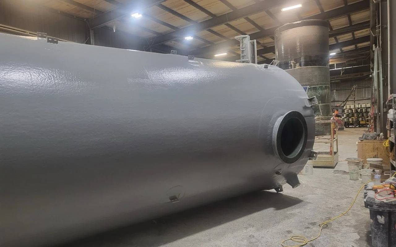 Large gray fiberglass storage tank under construction in an industrial facility, showcasing durable material and precision engineering for water and chemical storage.