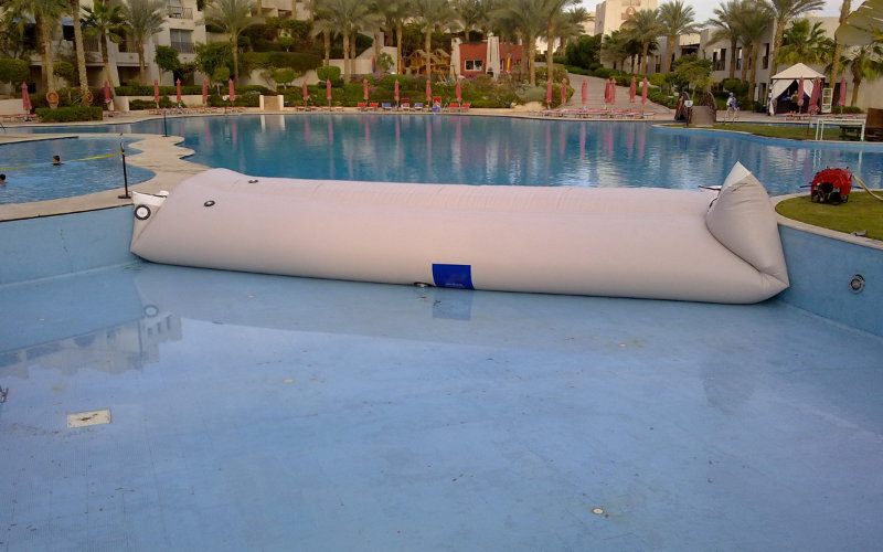 Inflatable white water bladder tank deployed in an empty pool for controlled water storage or liquid containment testing.