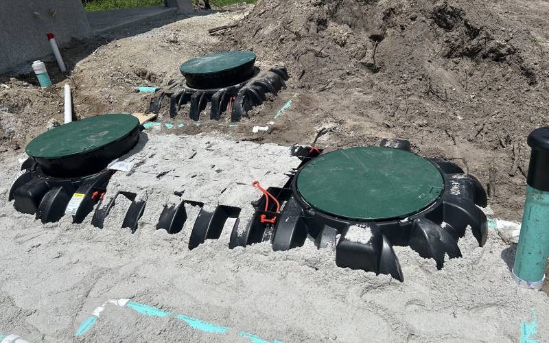 Two standard septic tanks installed underground with green access lids, surrounded by sand and plumbing connections
