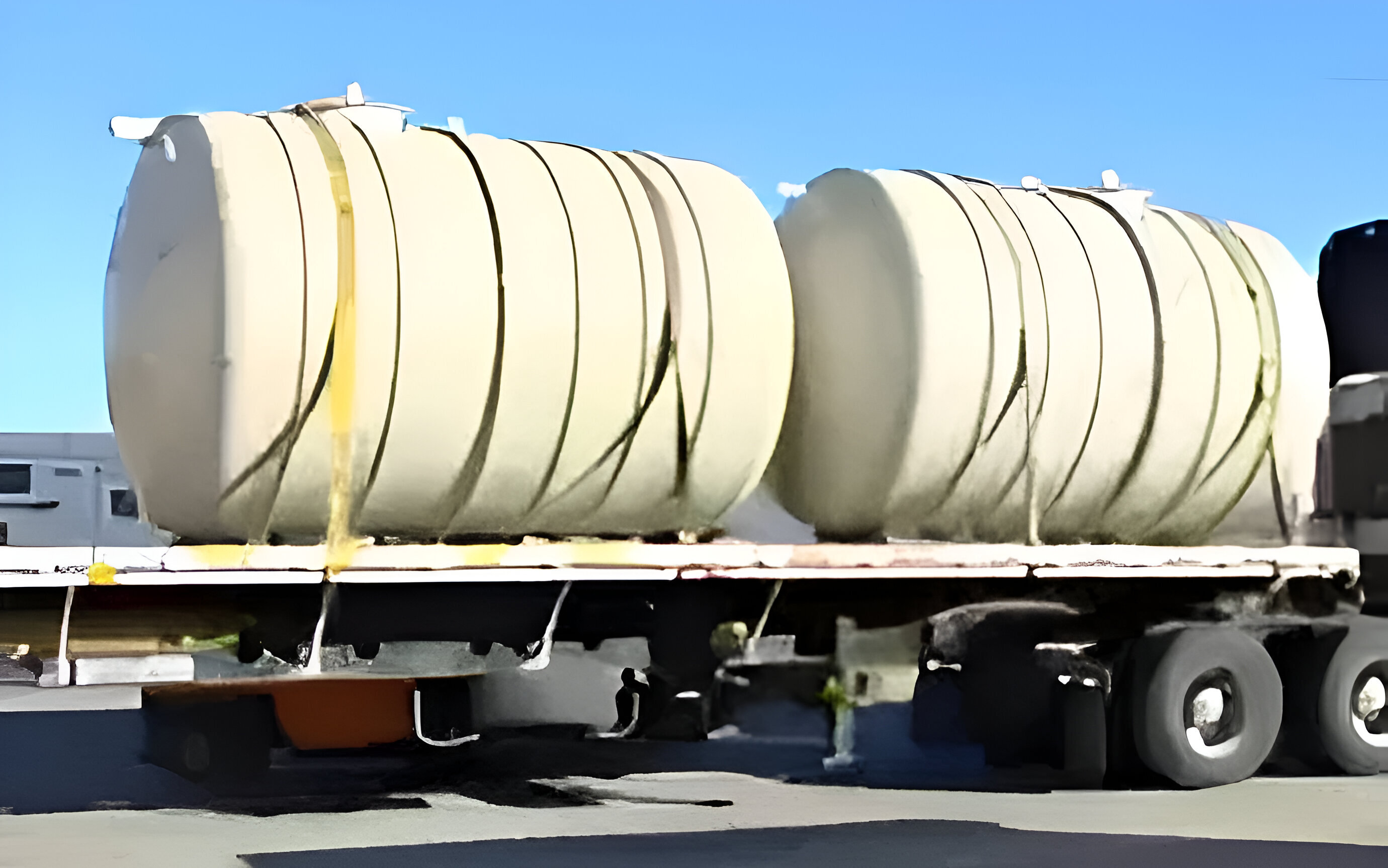 Two fiberglass water tanks secured on a flatbed trailer for delivery, ready for underground installation.