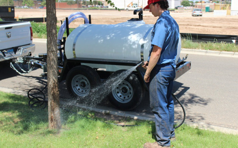 a man using the 550 gal to water a tree
