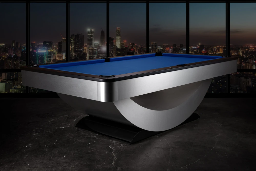 Three-quarter view of the Doc & Holliday Poshy Reverse Rainbow Slate Pool Table with Euro Blue Championship felt, matte black upper rails, and brushed metallic base, staged on a concrete floor with a modern backdrop wall.