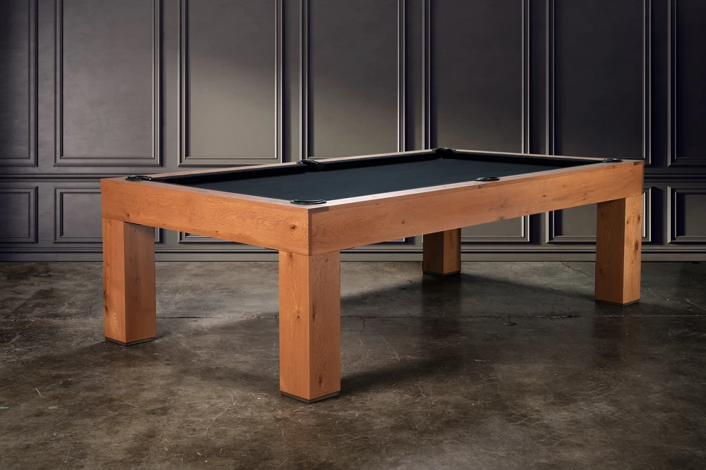 Doc & Holliday Parsons Pool Table in Rustic White Oak, three-quarter angled hero view. Photographed in a luxury interior with RH-style paneled walls and warm ambient lighting. Solid white oak frame with hand-weathered finish and clean Parsons silhouette, shown with black felt. Designed and made in the USA.