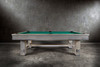 Side lifestyle view of the Churchill Pool Table in Smoked Maple with Championship felt, framed by a backdrop of polished cement flooring and warm neutral tones.