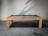 Side profile lifestyle image showcasing the Paula Parsons pool table in glazed maple finish, subtle distressed texture visible, modern concrete floor beneath, surrounded by a refined neutral space for luxury game room inspiration
