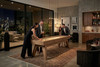Evening entertaining around the George shuffleboard table by Doc & Holliday in Glazed Maple, styled in a contemporary glass-wrapped interior with ambient pendant lighting, curated bar cabinetry, and architectural concrete walls highlighting the table’s warm maple grain and mid-century stance.