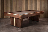 Three-quarter view of the Doc & Holliday Derby Slate Pool Table, crafted from solid walnut with maple inlay racing stripes along the pedestal legs and rails. The warm walnut finish paired with maple detail creates a bold, American-made design that stands out as both furniture and performance table.