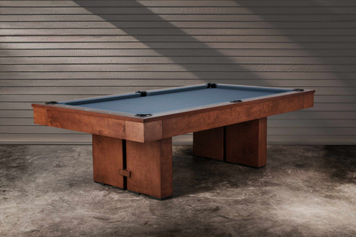 The Jackies slate pool table by Doc & Holliday, crafted in the USA from solid maple, styled in a modern interior. Shown in Bourbon Pecan Walnut finish with block pedestal legs and tapered rails, the table blends architectural presence with warm wood tones. Perfect for family gatherings or designer-curated lounges where performance and design belong together.