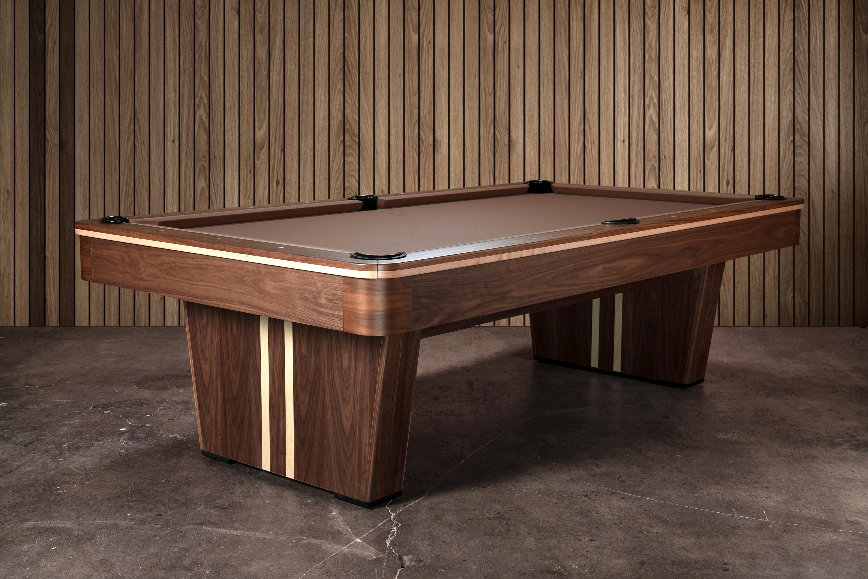 Three-quarter view of the Doc & Holliday Derby Slate Pool Table, crafted from solid walnut with maple inlay racing stripes along the pedestal legs and rails. The warm walnut finish paired with maple detail creates a bold, American-made design that stands out as both furniture and performance table.