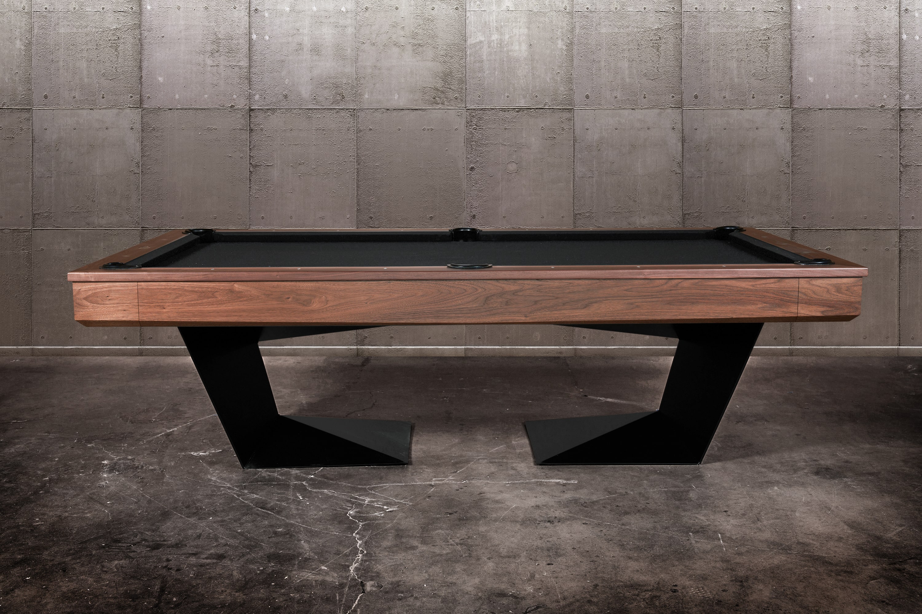 Side profile view of the Doc & Holliday TRON Pool Table featuring a handcrafted solid walnut wood top with visible natural grain | Industrial steel base in matte black with angular modern silhouette and precision slate bed | Photographed in a high-end interior setting | American-made billiards luxury by Doc & Holliday Billiards